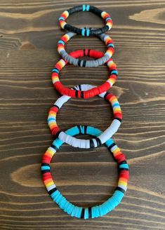 four bracelets with different colors and designs on them sitting on top of a wooden table