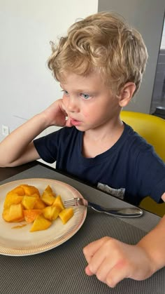 a little boy sitting at a table with some fruit on the plate in front of him