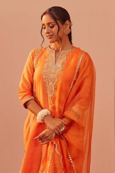 Tangerine orange kurta with tilla, patra, foil mirror embroidery in floral pattern. Paired with floral hand block print salwar and dupatta.
Components: 3
Pattern: Embroidery, Hand Block Printed
Type Of Work: Tilla, patra, foil mirror, floral
Neckline: Notched
Sleeve Type: Three quarter
Fabric: Kurta: Silk Chanderi, Salwar: Bamberg Satin, Dupatta: Silk Organza
Color: Orange
Other Details: 
Scallop bordered sheer dupatta
Lace embroidered cutwork hem
Occasion: Sangeet - Aza Fashions Dupatta Lace, Blouse Yoke, Mirror Embroidery, Personal Shopping Service, Embroidery Hand, Tangerine Orange, Organza Dupatta, Silk Organza, Cut Work