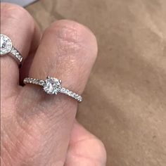 a woman's hand holding two engagement rings with diamonds on each one and the other side