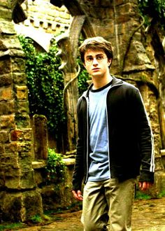 a young man standing in front of a stone building with ivy growing on the walls