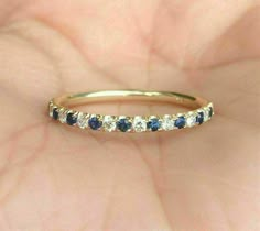 a woman's hand holding a gold ring with blue and white stones on it