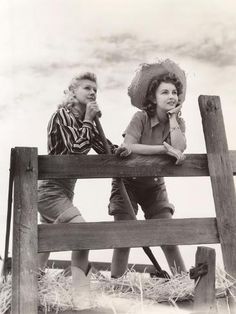 an old photo of two women sitting on a wooden fence eating something out of her mouth