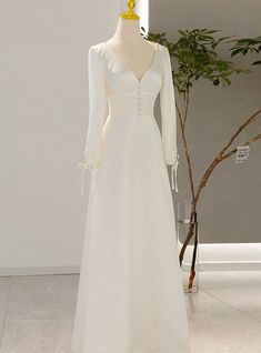 a white wedding dress on display in a room next to a potted green plant