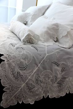 an unmade bed with white linens and lace on the comforter is shown