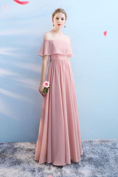 a woman in a long pink dress standing against a wall with her hands on her hips