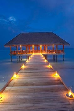 a wooden dock with lit candles on it and a thatched roof over the water