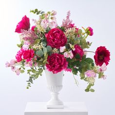 a white vase filled with lots of pink and red flowers on top of a table