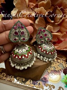 Looking for a one of a kind meenakari handpainted STATEMENT set of jhumka style earrings and doesn't hurt your ears, look no further! This lightweight  brass-based textured silver tone finish jhumka style earrings has a very contemporary style with multi colors painted work encompassed with pearl embellishments at the bottom of earrings. There are two variations to this piece: One that has green/red stones while the other has a clear stones.  The combination of the stone work with a silver tone painted brass-based metal finish will surely make you get those well-deserved jaw-dropping attention. It's the right balance you need to make a statement but not over the top.     Highlights of the piece: ** Dangled full jhumka style earrings with height: 3.25 inch ** Pushback in the back for the ea Traditional Kundan Jhumkas With Oxidized Finish, Festive Oxidized Finish Round Jhumkas, Festive Green Oxidized Earrings, Festive Silver Dual-tone Jhumkas, Traditional Dual-tone Metal Jhumkas, Jhumkas Earrings, Top Highlights, Carved Jewelry, Paint Brass