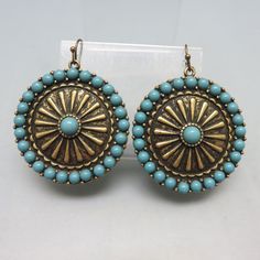 These pretty Mandala shaped earrings are inlaid with pieces of fairly realistic looking faux turquoise set into goldtone metal. They measure  2 inches long (including the wires)  and 1 5/8th inch wide . They have a mandala, wagon wheel design and are light and comfortable on.  They are in MINT condition with no markings. This will arrive in a lovely gift box for easy gift giving or safe storage.  For more pieces of vintage costume jewelry, old silver, bolo ties and vintage accessories, kindly ch Blue Concho Dangle Earrings, Turquoise Concho Dangle Jewelry, Bohemian Turquoise Concho Earrings, Festival Concho Dangle Jewelry, Southwestern Concho Earrings For Festivals, Turquoise Nickel-free Southwestern Earrings, Nickel-free Turquoise Southwestern Earrings, Turquoise Brass Jewelry With Ear Wire, Bohemian Concho Dangle Jewelry