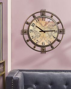 a large metal clock mounted to the side of a wall next to a gray couch