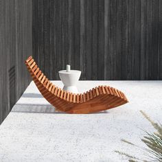 a white vase sitting on top of a wooden bench next to a wall and grass