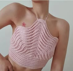 a woman wearing a pink crop top with crochet on her chest and one hand on her hip