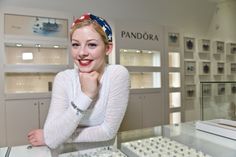 a woman standing in front of a display case with jewelry on the shelves behind her