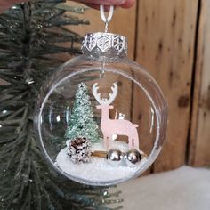 a glass ornament with a deer and pine tree inside it, hanging from a christmas tree