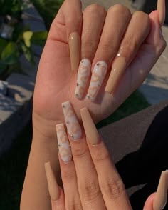 a woman holding up her nails with white and beige designs on the tip of their fingers