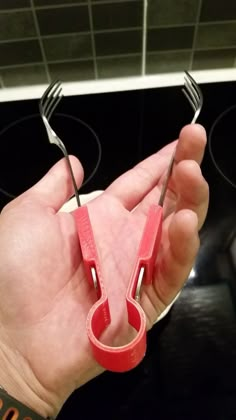 a hand holding two pairs of scissors in front of a stove top with the handles still attached