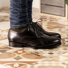 a close up of a person's shoes on the ground with tiled flooring