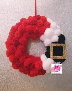 a red and white christmas wreath hanging from the ceiling with a gold buckle on it