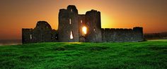 the sun is setting over an old castle on top of a hill with green grass