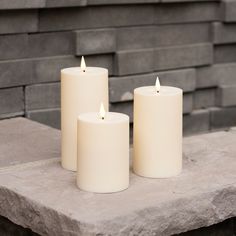 three white candles sitting on top of a stone slab