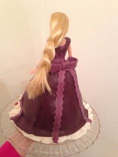 a barbie doll sitting on top of a cake with long blonde hair in a purple dress