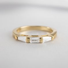 a yellow gold ring with two baguettes on the side, sitting on a white surface