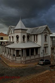 a large white house sitting on the side of a road next to tall buildings under a cloudy sky