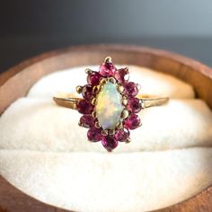 This beautiful vintage 9ct gold ring features a striking marquise-cut opal surrounded by a vibrant halo of pink sapphires, creating a captivating and elegant piece. The opal center stone shimmers with iridescent colors, while the surrounding pink sapphires add a charming contrast that enhances the ring's timeless beauty. The delicate detailing and unique cluster design make this ring a perfect choice for anyone who appreciates vintage jewelry with a touch of color and sophistication. Ideal for special occasions or as an everyday statement piece, this ring is sure to draw compliments and become a cherished addition to any collection. It also makes a wonderful gift for a loved one who adores vintage and gemstone jewelry. Material: 9ct Gold Main Stone: Marquise-cut opal Accent Stones: Pink sa Engagement Ring Victorian, Vintage Opal Engagement Ring, Victorian Engagement Rings, Cluster Design, Saphir Ring, Adored Vintage, Ring Marquise, Opal Engagement Ring, Pink Sapphire Ring