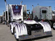 two large semi trucks parked next to each other in a parking lot with people looking at them