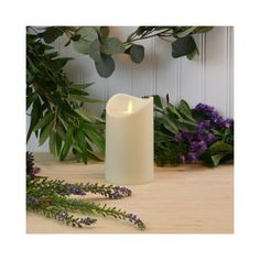 a white candle sitting on top of a wooden table next to purple flowers and greenery