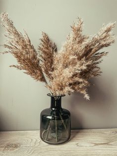 some dried plants in a black vase on a table with a gray wall behind it