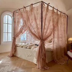 a canopy bed with sheer curtains on top of it in a bedroom next to a window