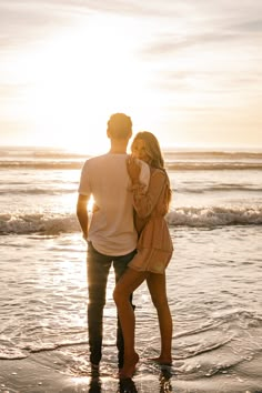 a man and woman standing on the beach at sunset with their backs to each other