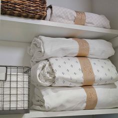 towels and blankets are stacked on top of each other in a white shelf next to a basket