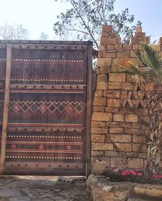 a wooden gate sitting next to a brick wall with flowers growing out of it and a palm tree in the background