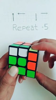 two hands holding a rubik cube in front of a white paper with the word repeat 5 written on it