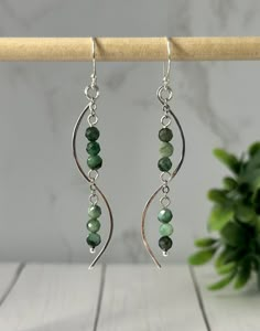 the earrings are made with green beads and silver wire, hanging from a wooden stick