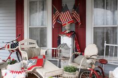 an american flag is hanging on the front door of a house with two chairs and a bicycle