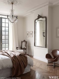 a bedroom with a chandelier, mirror and chair in it's corner