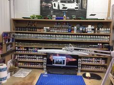 a laptop computer sitting on top of a wooden desk next to shelves filled with paint