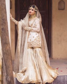 a woman in a white and gold bridal outfit standing on steps with her arms outstretched