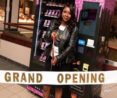 a woman standing in front of a vending machine holding a sign that says grand opening