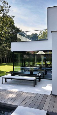 an outdoor patio with tables and benches next to a pool in front of a house