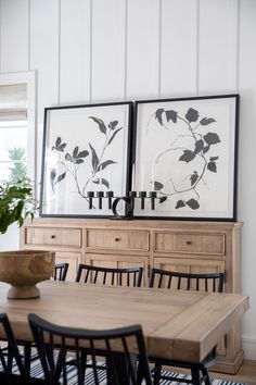 a dining room table with chairs and two pictures on the wall