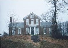 an old red brick house sitting on top of a hill in front of some trees