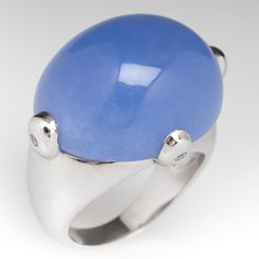 This wonderful ring is centered with an oval, blue chalcedony cabochon, weighing 30.00 carats, set in a four-prong setting. Each prong is flush set with one (1) round brilliant cut diamond. The ring measures 19.7mm at the top, rises 12.8mm above the finger, tapering to 3.4mm wide and 0.9mm thick at the base of the shank. This ring is currently a size 6.5. Modern Oval Cabochon Dome Ring, Modern Dome Ring With Oval Cabochon And Polished Finish, Modern Dome Ring With Polished Oval Cabochon, Modern Cabochon Moonstone Ring For Formal Occasions, Modern Oval Cabochon Moonstone Ring For Formal Occasions, Modern Moonstone Ring With Oval Cabochon, Modern Dome Ring With Oval Cabochon For Formal Events, Formal Blue Oval Cabochon Moonstone Ring, Modern Oval Cabochon Moonstone Ring