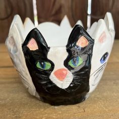 a black and white cat head with green eyes on top of a wooden table next to two candles