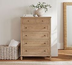 a white vase sitting on top of a wooden dresser next to a mirror and wicker basket