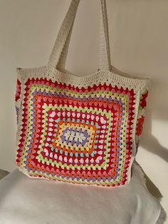 a crocheted bag hanging on a wall with a white pillow in the background